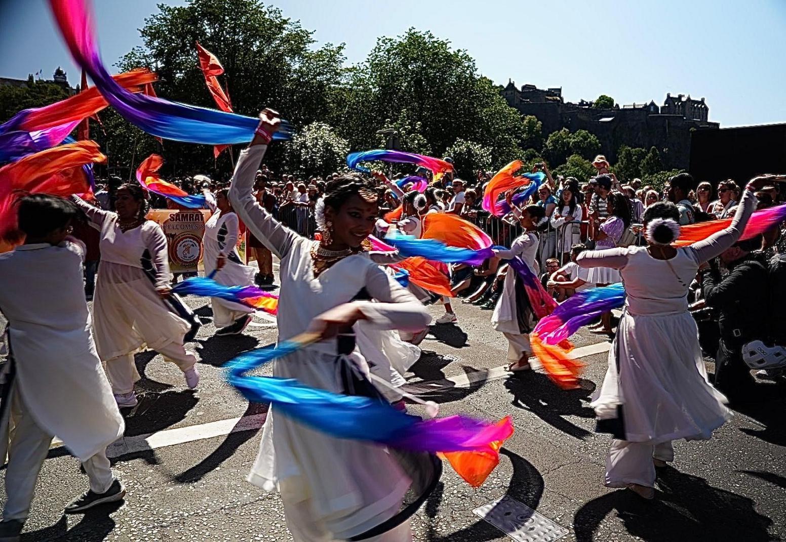 Dancers in white waving coloured ribbons in a sunlit street parade