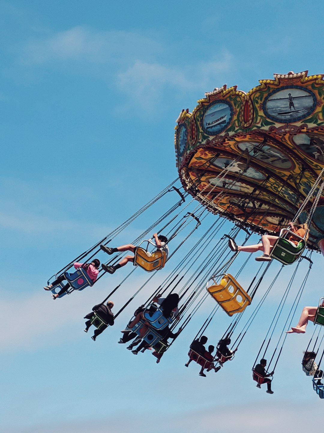 People riding an ornate golden wave swinger against a bright blue sky