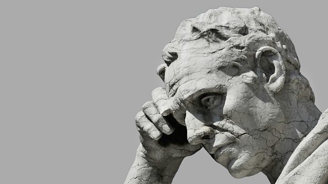 A weathered stone statue of a man resting his head on his hand in thought