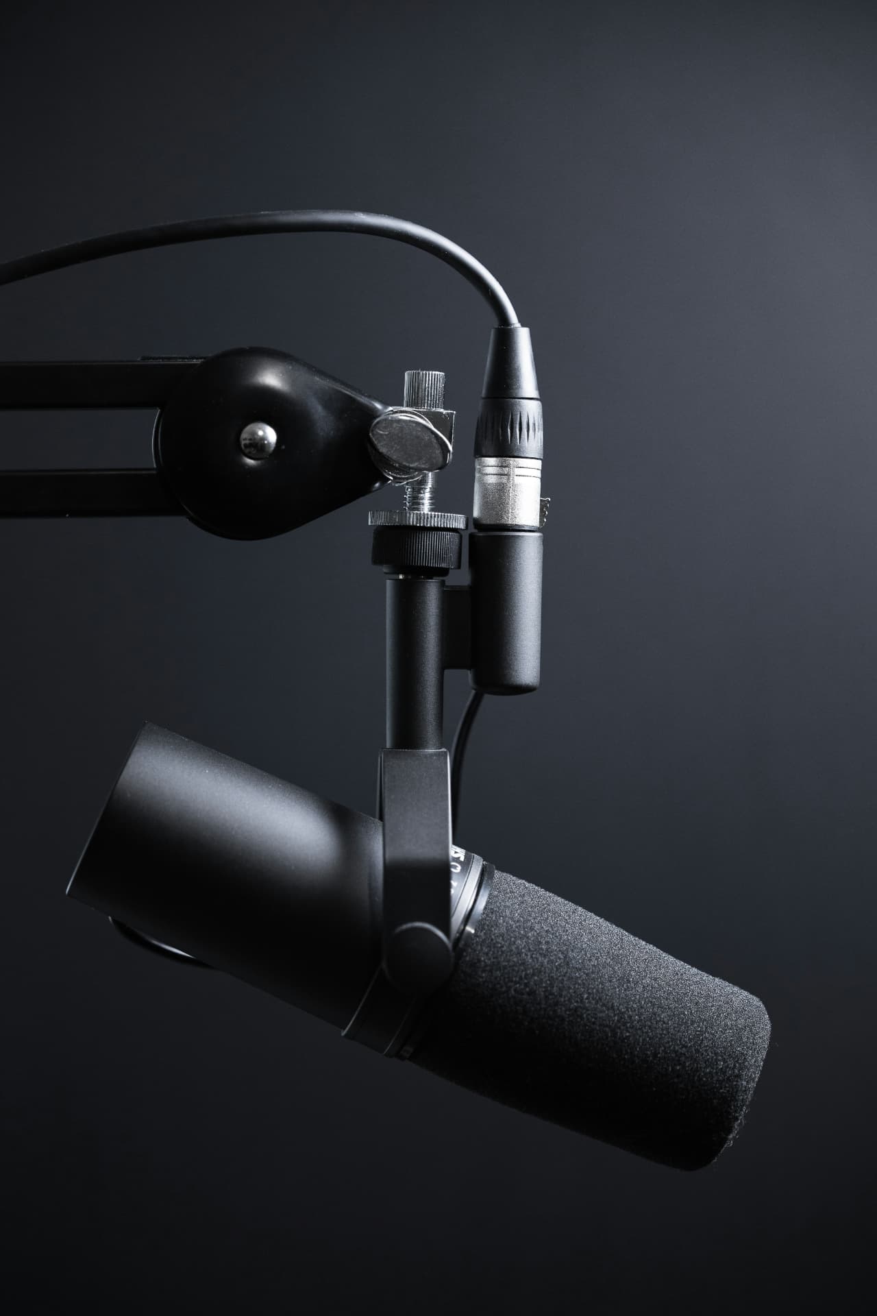 A broadcast microphone on a boom arm against a dark studio backdrop