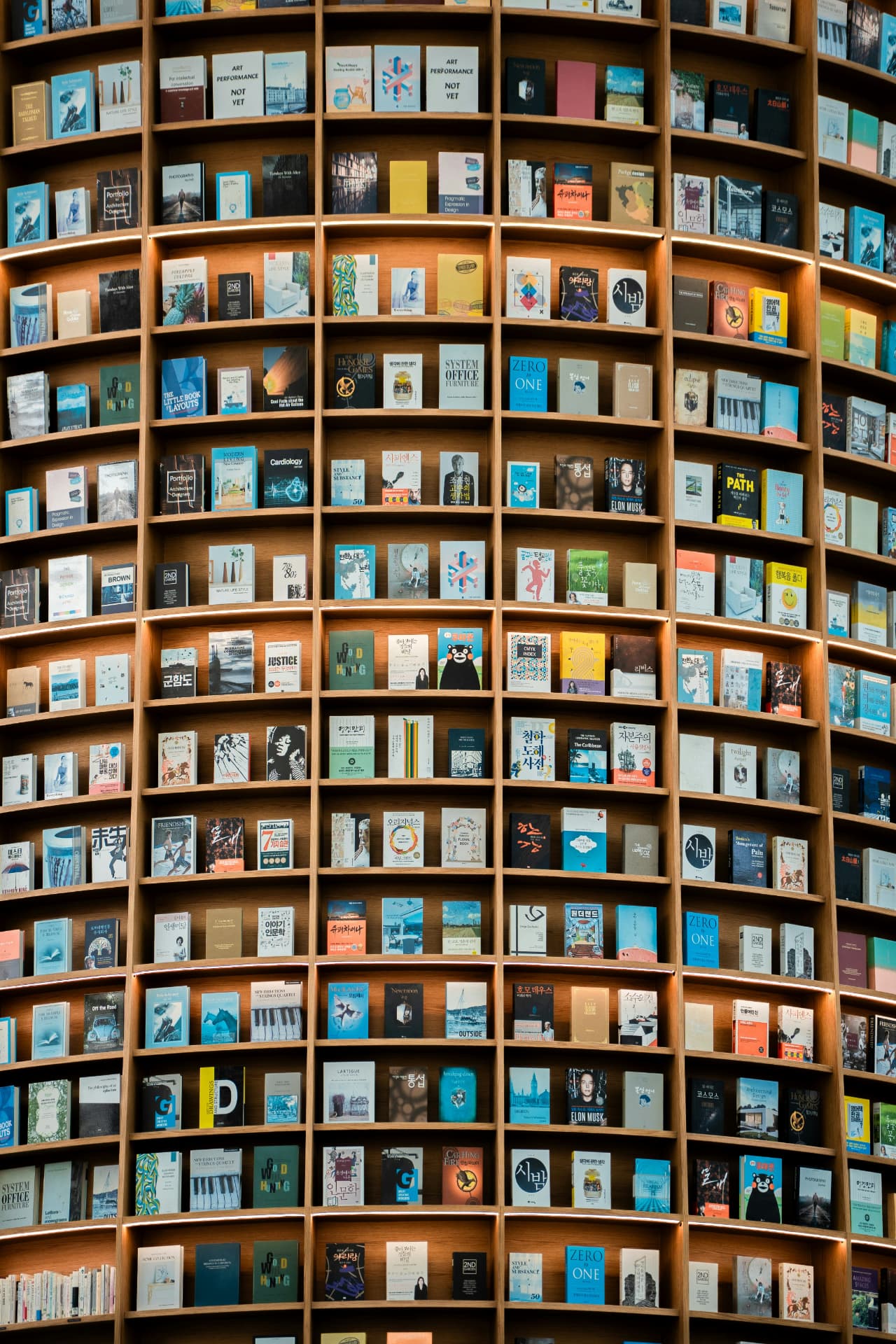 A tall wooden shelving unit filled with hundreds of books displayed cover outward in a modern library