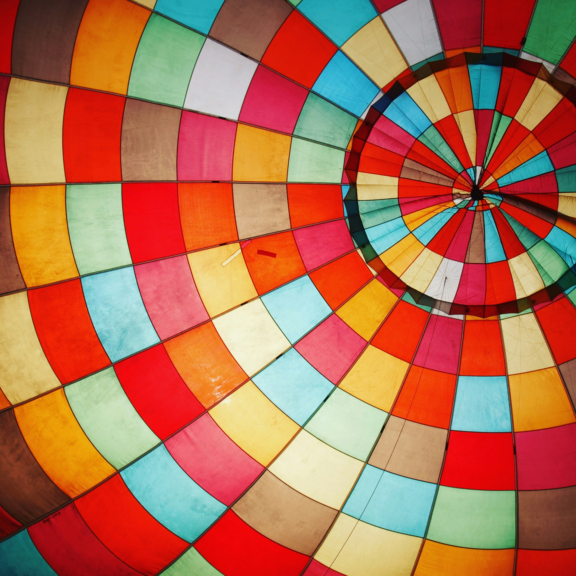 The inside of an inflated hot air balloon canopy, panels of red, orange, yellow, blue and green converging to the apex