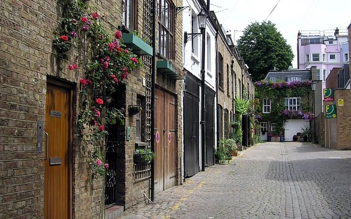 A quiet cobblestone mews street lined with brick homes dressed in climbing roses
