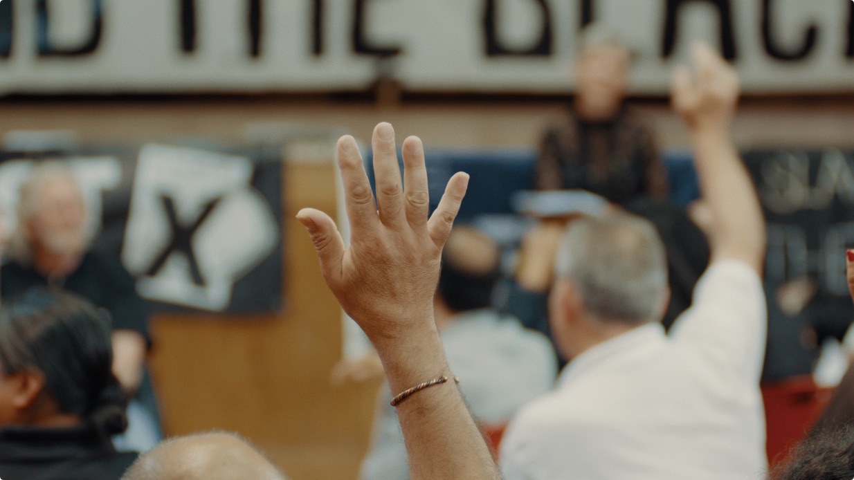 A raised hand among an audience at an indoor community meeting